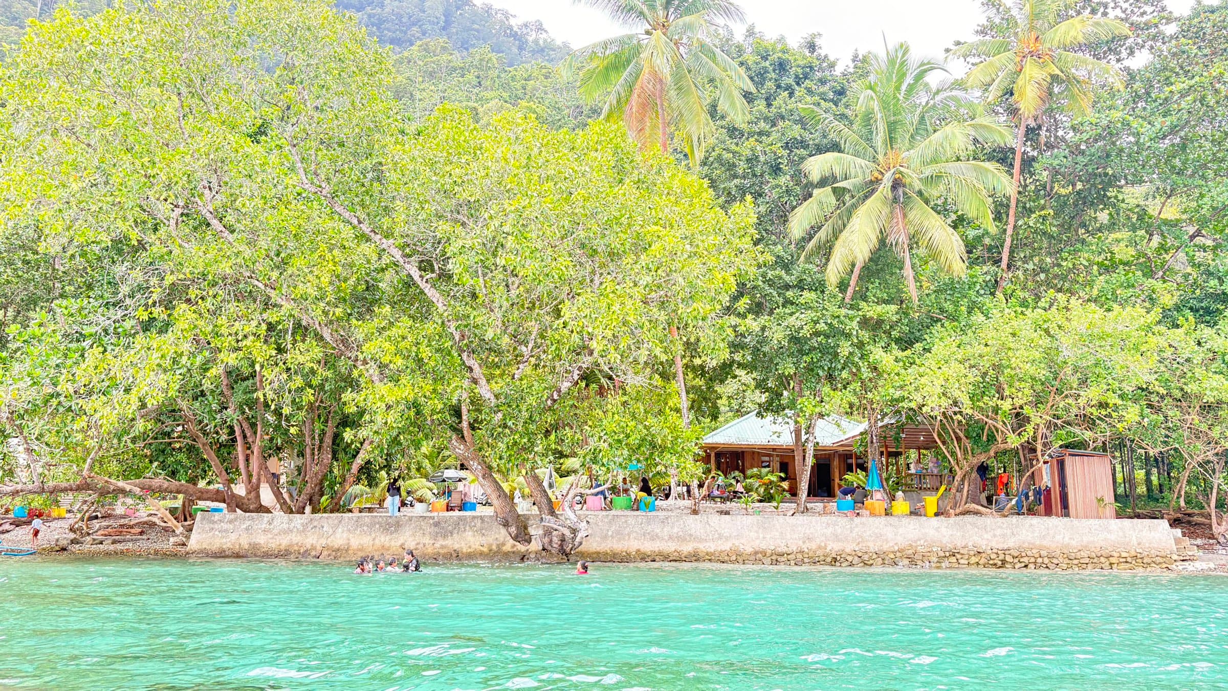 Air laut jernih kehijauan Pantai Memit dengan cottage dan gazebo di tepi hutan Morella, Shafira Resort