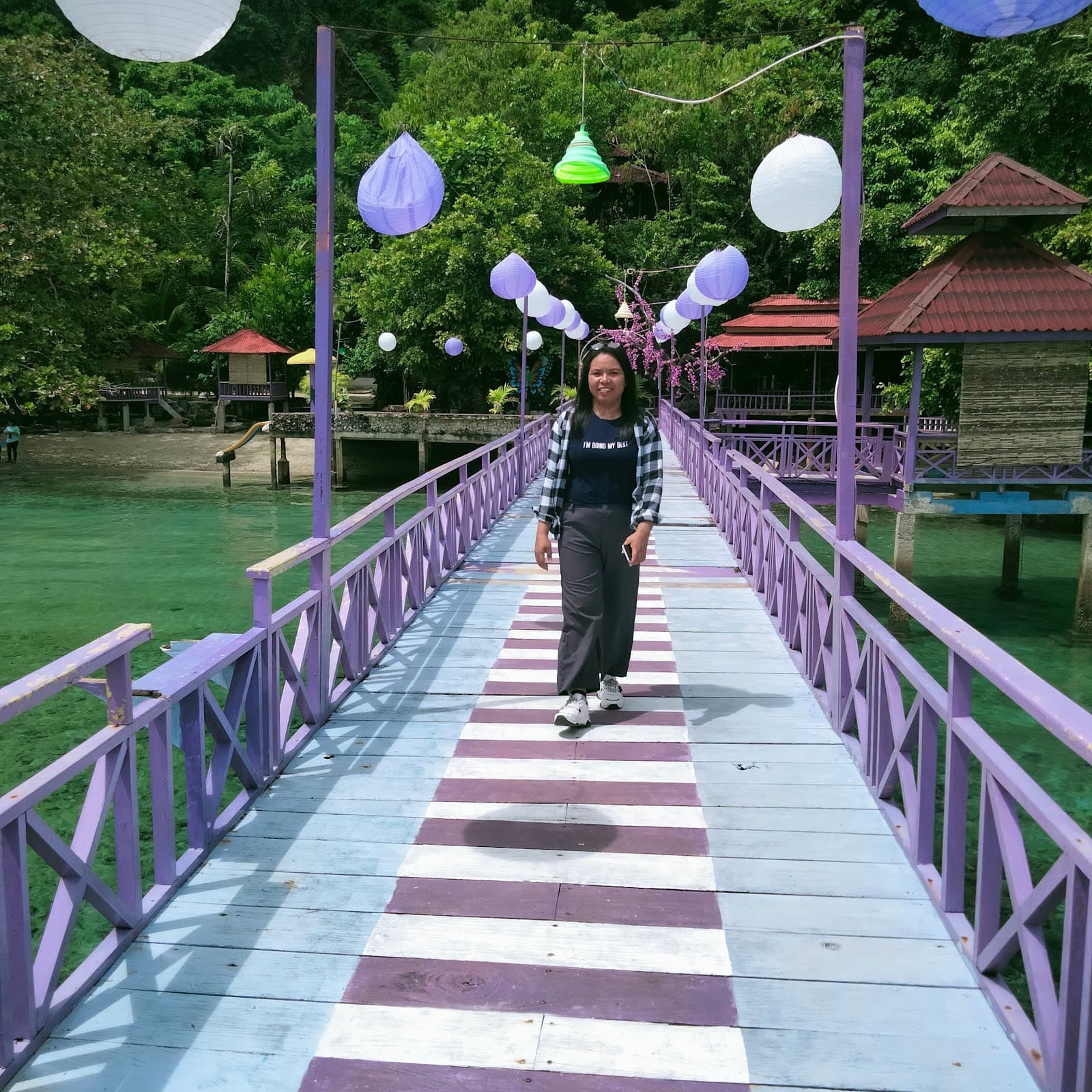 Dermaga kayu ungu Shafira Resort berhias lampion dengan gazebo di atas air laut jernih