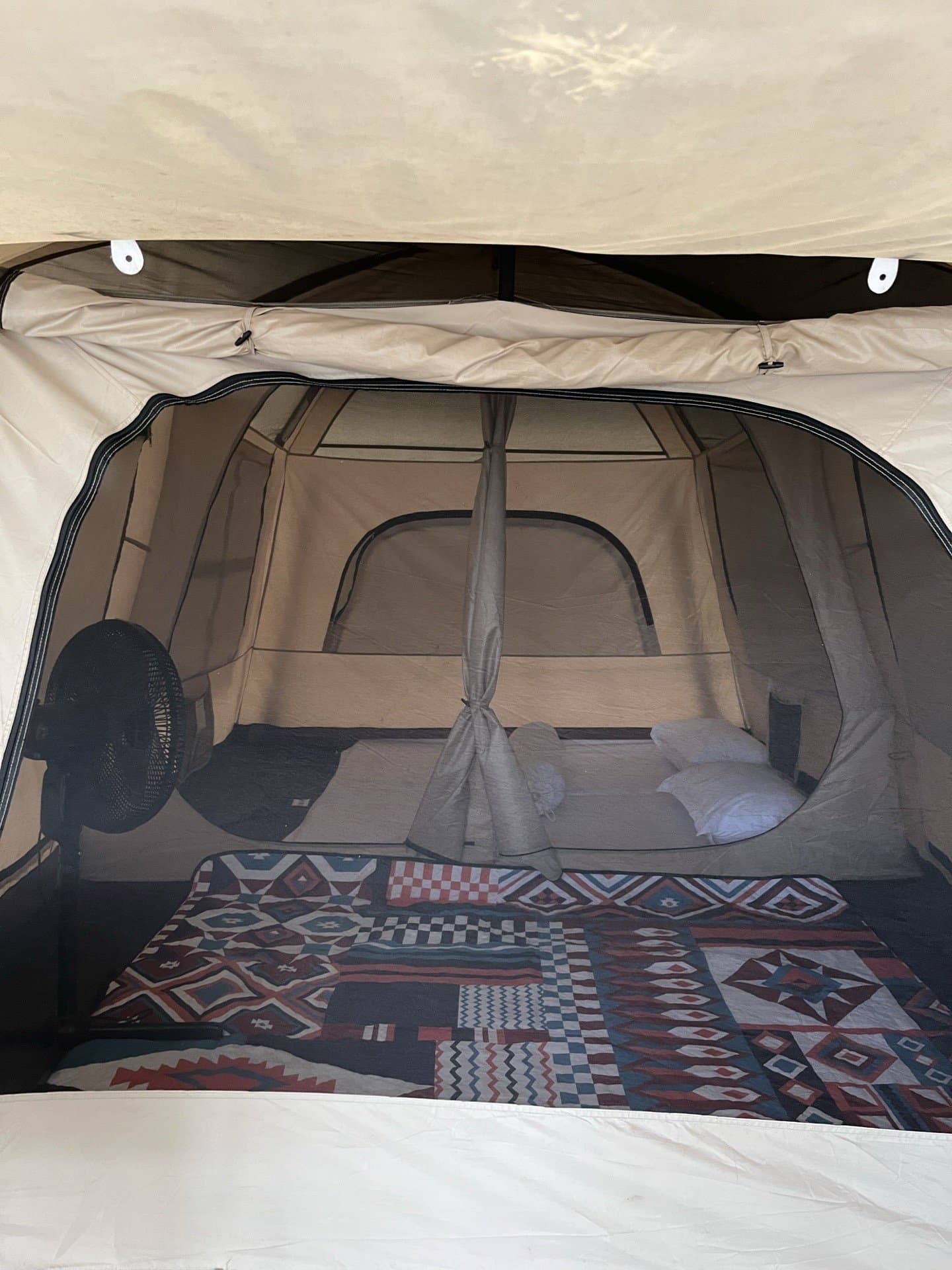Interior tenda glamping Shafira Resort dengan kasur, kipas angin, dan alas bermotif
