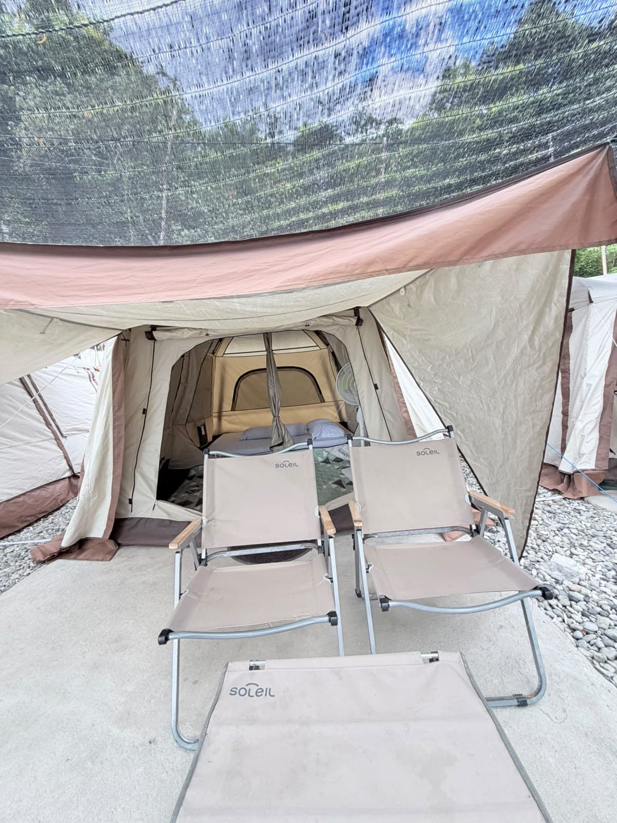 Kursi santai dan meja lipat di depan tenda glamping Shafira Resort di bawah jaring peneduh