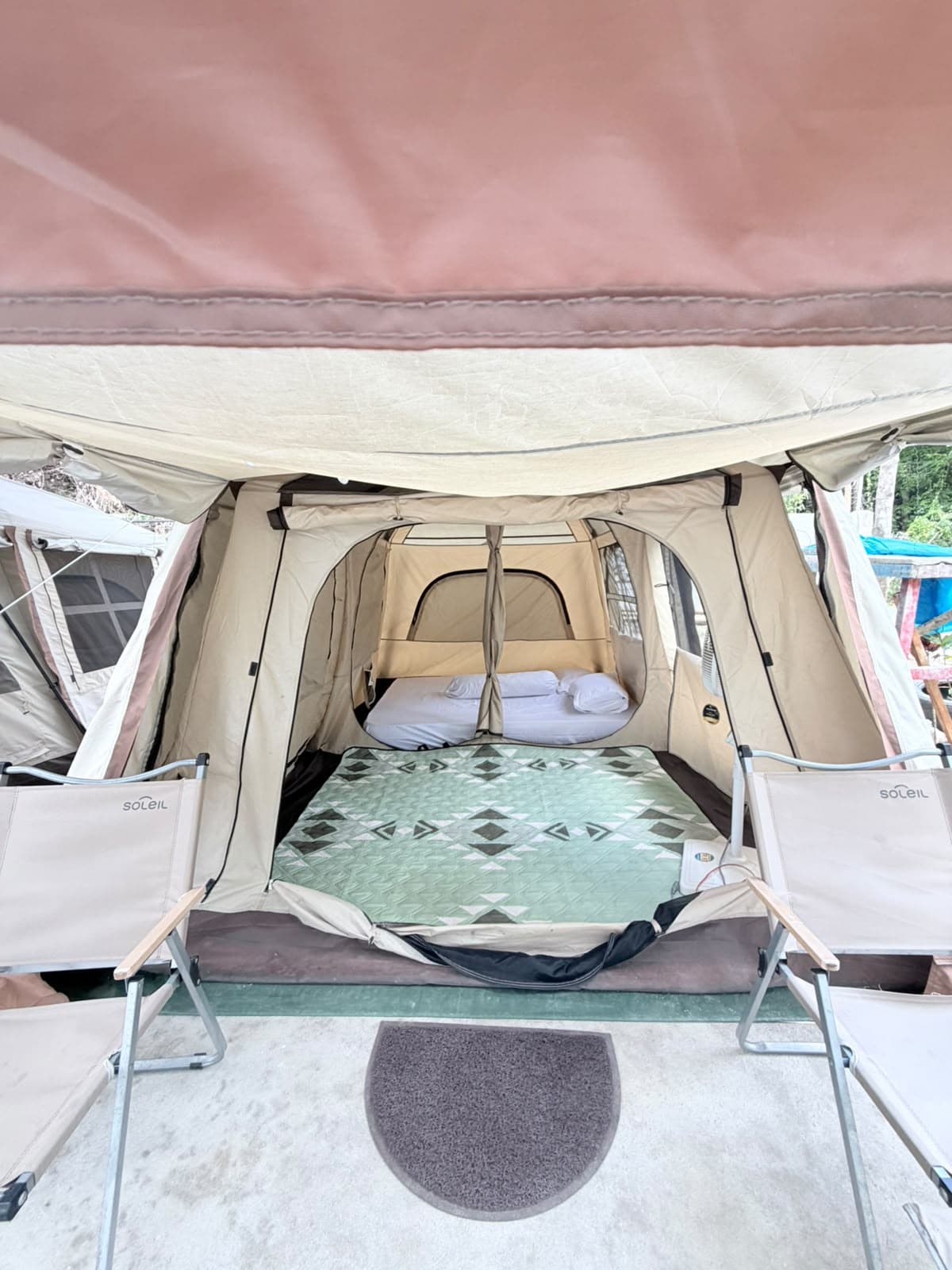Teras tenda glamping Shafira Resort dengan dua kursi santai dan keset di depan pintu tenda