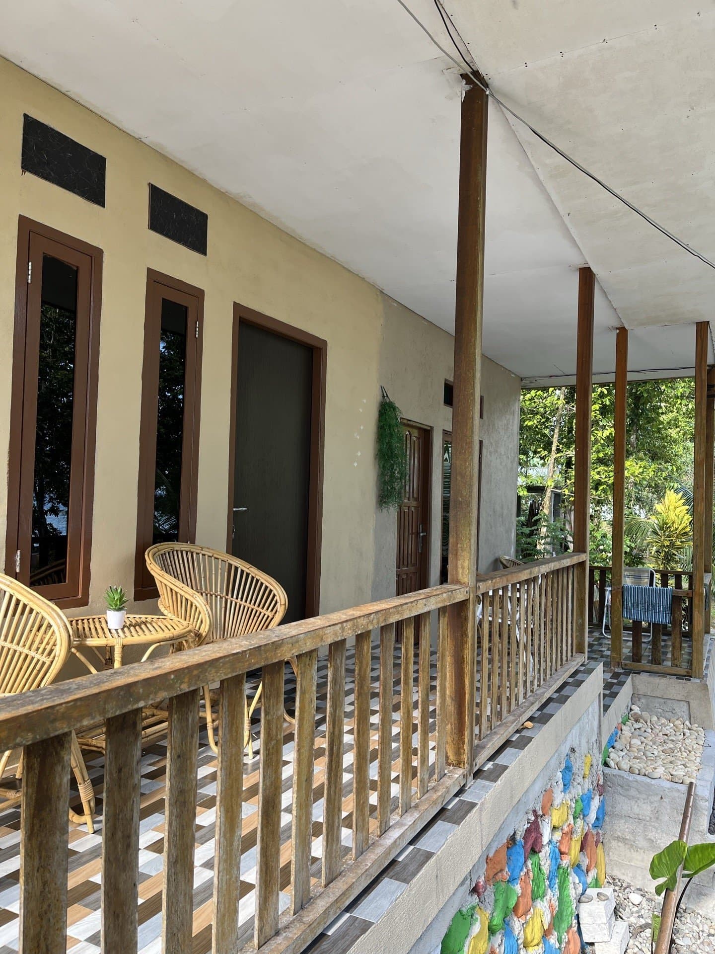 Room terrace at Shafira Resort with rattan chairs, wood-framed windows, and a colorful stone garden on Memit Beach, Morella
