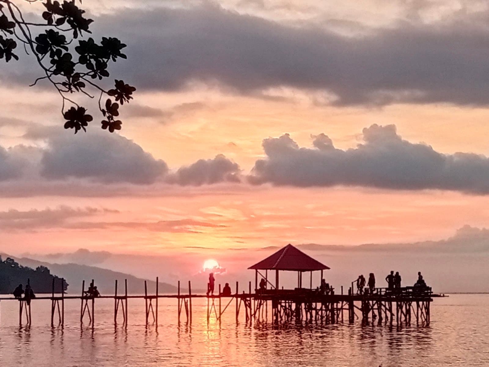 Matahari terbenam jingga di balik dermaga dan gazebo Shafira Resort, Pantai Memit Morella